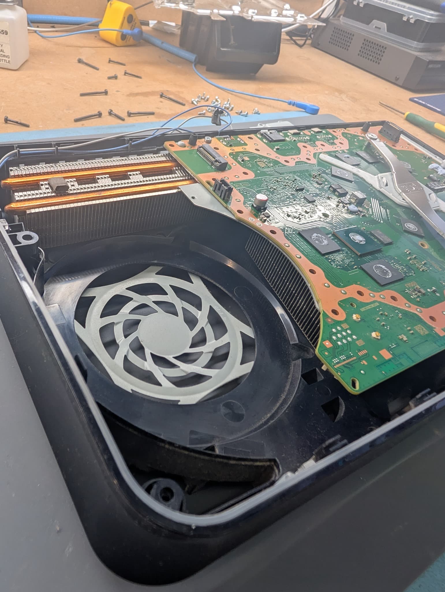 Disassembled game console revealing its internal cooling fan, copper heat pipes, and green motherboard.
