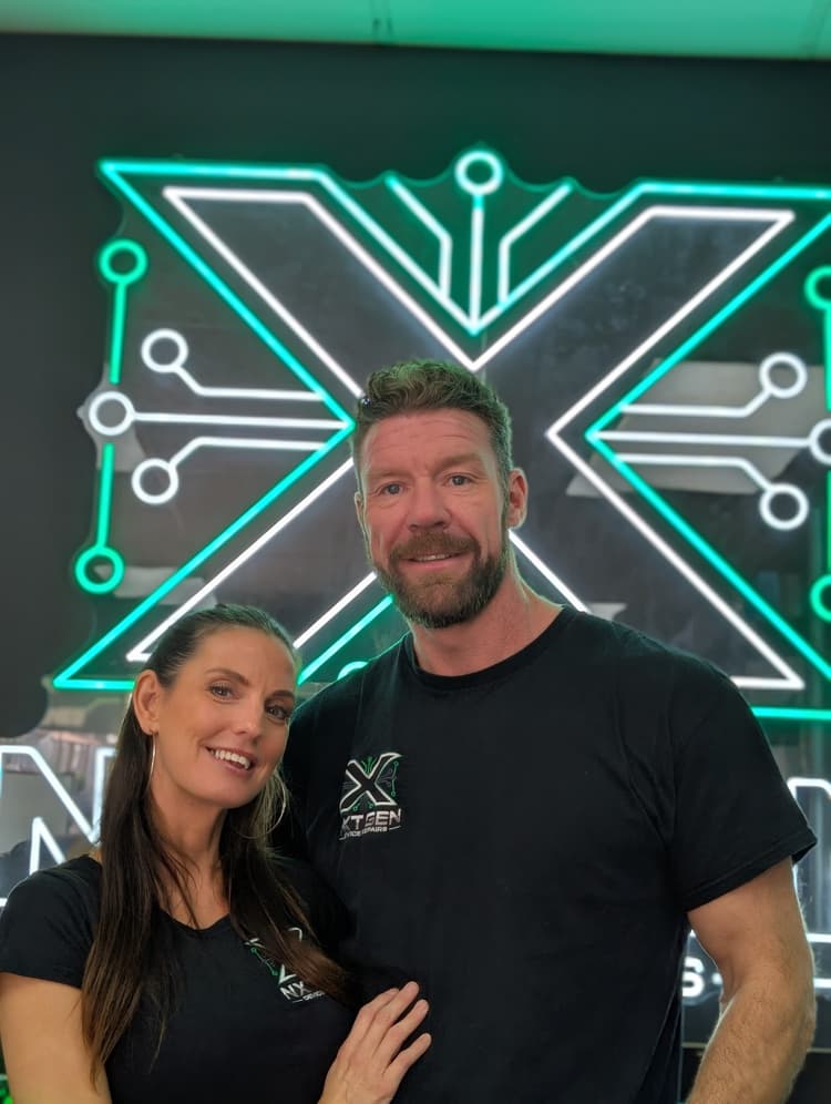 Jon and his wife in NXT GEN shirts in front of the illuminated shop logo